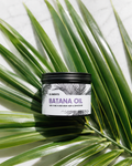 Jar of batana oil on a green palm leaf with El3ments Skincare label