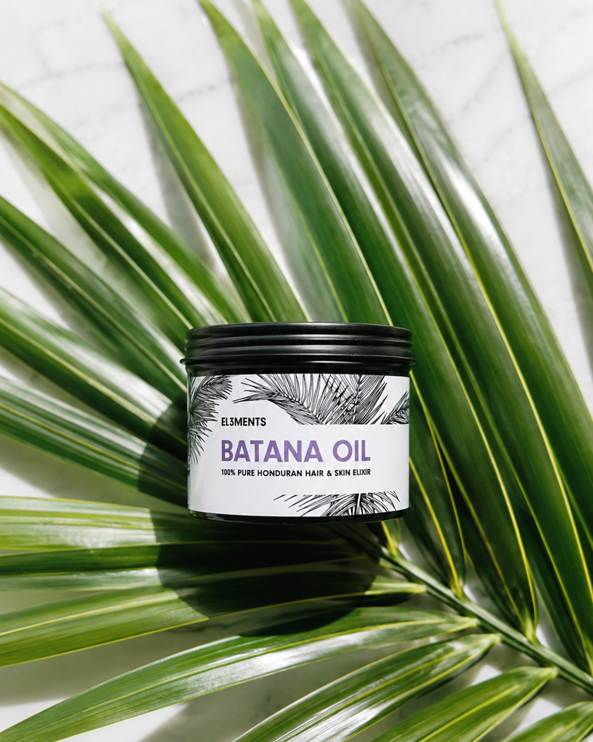 Jar of batana oil on a green palm leaf with El3ments Skincare label