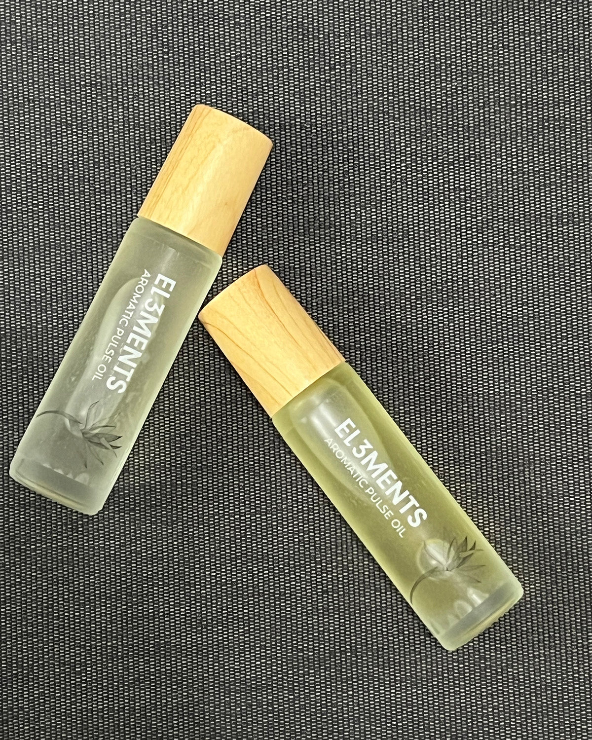 Two small fragrance oil bottles labeled El3ments on a textured gray background