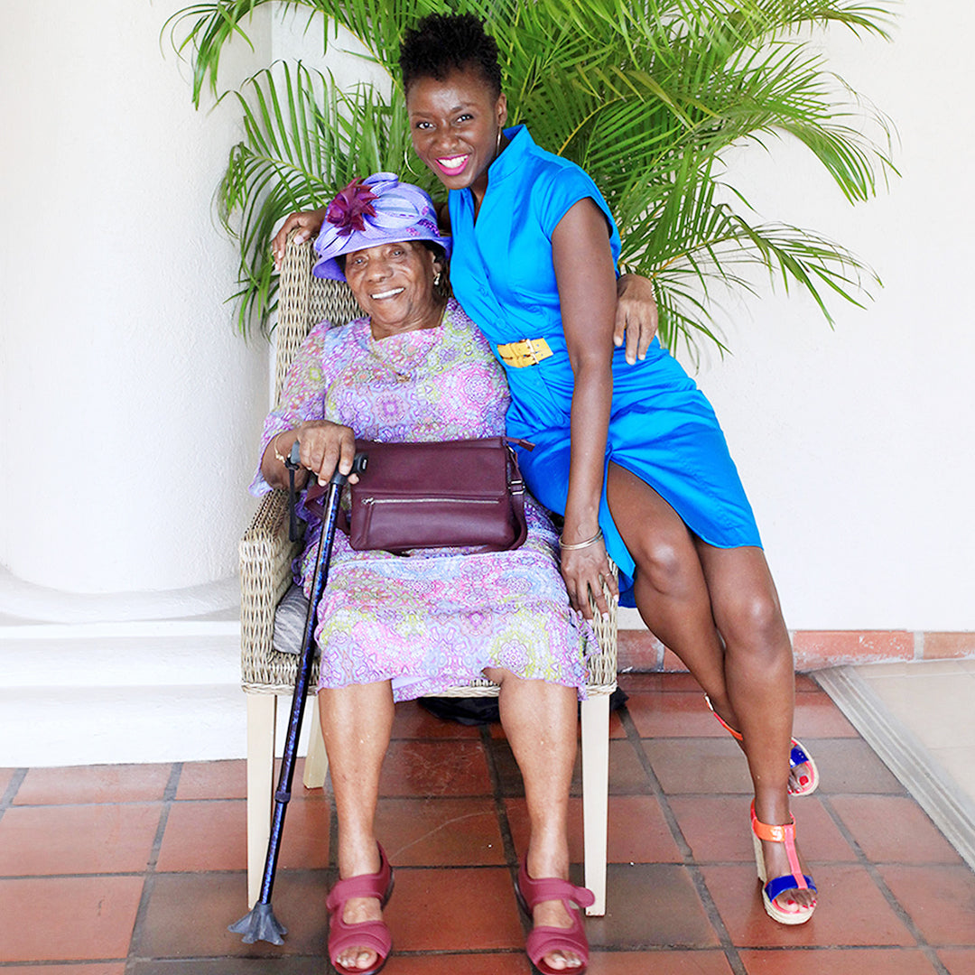 Two smiling women sitting together at a birthday event in Barbados with a palm tree background against white