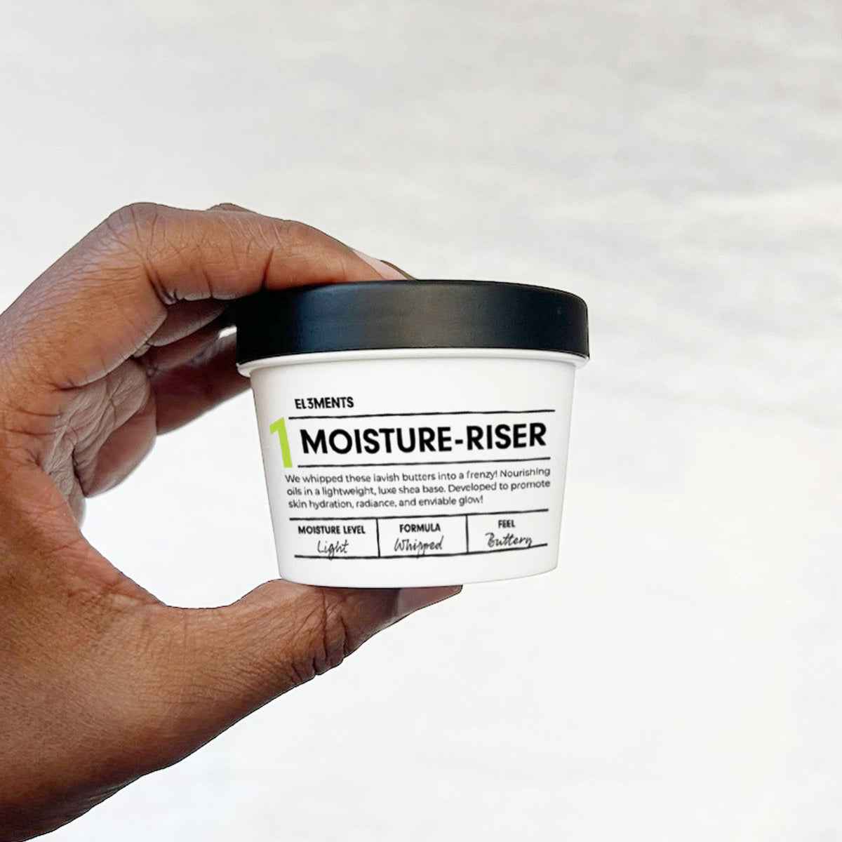 Hand holding MOISTURE-RISER Body Butter demi jar on white background