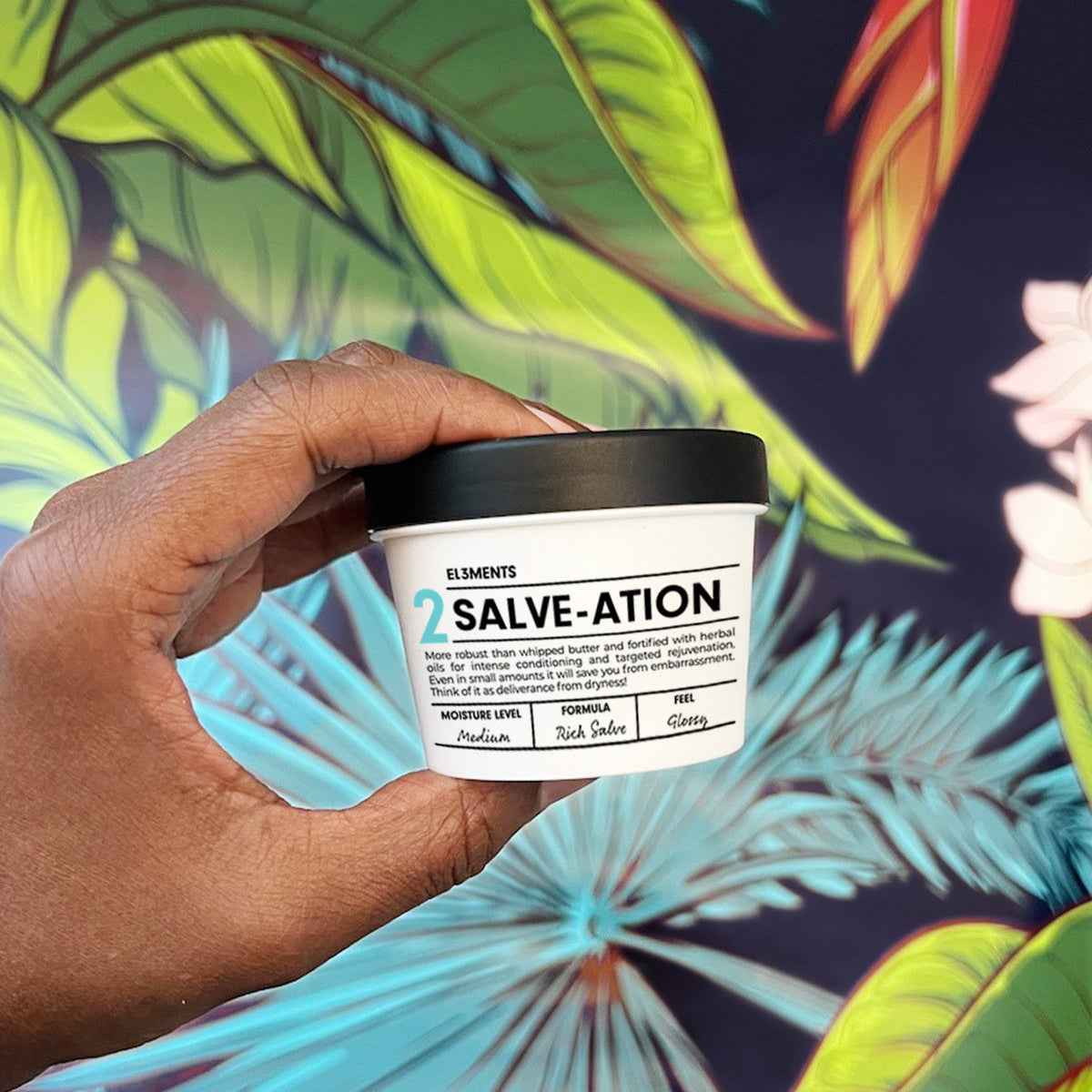 Hand holding Salve-ation Body Butter demi jar on tropical background