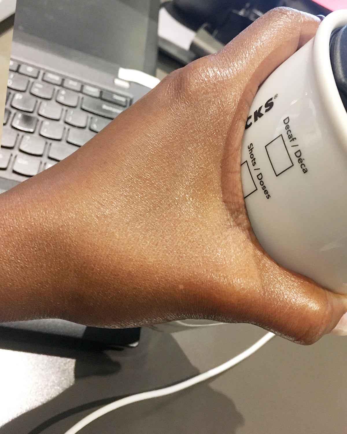 Hand holding a coffee mug with text in an office setting